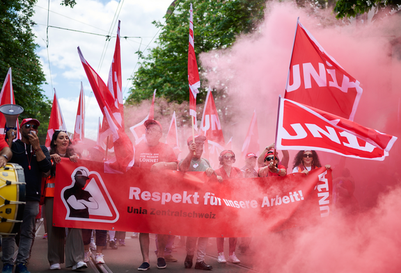 Demonstrierende der Unia Zentralschweiz mit roten Unia-Fahnen fordern auf einem Transparent mit der Aufschrift «Respekt für unsere Arbeit!» bessere Arbeitsbedingungen.